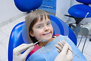 A lovely little girl sitting in a dental chair in hospital. A child dentistÃ¢â¬â¢s hands. A little girl sitting at the dentistÃ¢â¬â¢s photo